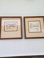 Photo of the pair of framed etchings showing rural scenes with houses and fields, both signed and numbered.