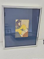 Framed pastel drawing in silver metal frame with dark blue mat, displayed on white surface