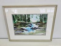 Framed watercolour painting showing the full artwork depicting a creek in a forest setting.