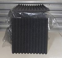 Black acoustic foam panels with pyramid and ridged textures stacked and sealed in plastic bags against a metallic background.