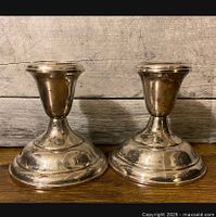 Front view of both sterling silver candle holders placed side by side on wooden surface against textured grey background.