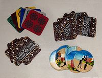 Four sets of African themed coasters arranged on a table, showing round and square shapes with painted village scenes and tribal patterns.