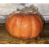 Front view of large pumpkin-shaped candle wrapped in clear plastic with tied string.