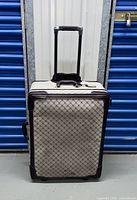 Front view of the beige patterned Ralph Lauren suitcase with extendable handle and brown leather corner reinforcements.