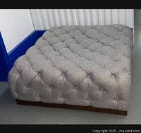 Side view of large tufted ottoman showing deep button tufting on fabric upholstery and dark wooden base.