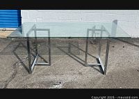Full view of modern glass top dining table showing clear glass surface and chrome metal base with geometric leg design.