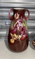 Maroon vase with floral pattern and two handles shown against a metal background