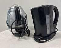 Two electric kettles on a white surface, one black plastic kettle and one vintage General Electric metal kettle with cord wrapped around base.