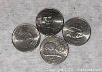 Photo shows four different US 5 cent coins on fabric background: one with American bison, one with Jefferson Memorial, one showing two hands shaking, and another with indistinct design.