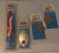 Four Lucky Strike fishing accessories including two #2 Canoe lures, one Silver Lake spinner blade, and two Rudder Flash spinner blades, all new in factory packaging.