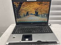 Front view of Acer Aspire 9300 laptop with screen on showing a wallpaper with fall foliage and pathway.
