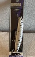 Photo showing one factory packaged Balkan Minnow floating fishing lure with silver spotted design, hooks attached, and packaging visible