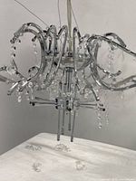 Front and side views of the modern silver metal chandelier frame with hanging crystal beads. Loose crystal pieces visible on the table surface near the base.