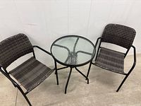 Front view showing two dark gray woven rattan-style chairs and round glass-top table.