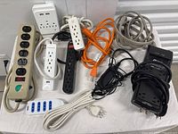 Various power strips, extension cords, and charging adapters arranged together on a floor, showing quantity and condition.