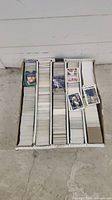 White corrugated storage box with thousands of baseball cards arranged in five compartments. Some cards are stacked and scattered on top of the cards.