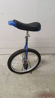 Side view of the blue 20 inch unicycle showing padded black and blue saddle, knobby tire, and plastic pedals.