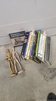 Art books and two wooden artist mannequins placed on ground