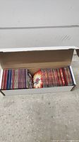 White cardboard box filled with multiple stacks of Bakugan trading cards, showing various fronts and backs of cards across a long box.