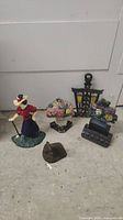 Photo showing all five cast iron door stops together on floor: woman figure, floral basket, lantern, book stack with flowers, and shoe shape.