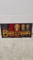 Full front view of Babushka Dolls slot glass with colorful text and three doll illustrations.