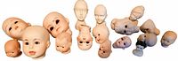 Photo showing all 18 vintage porcelain doll heads arranged in a row, displaying various facial features and sizes.