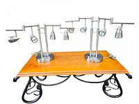 Two silver-colored adjustable spotlight table lamps on a wooden surface with a decorative metal base, showing front and side angles. Each lamp has four bulbs and a round base.