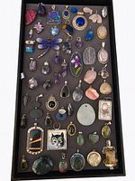 Overview tray of 56 gemstone pendants in various shapes and colors on black background.