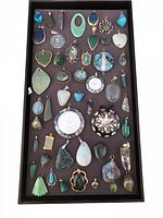Black tray displaying 86 assorted gemstone pendants in various shapes and colors