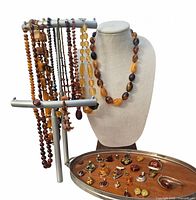 Silver display stand holding eight amber bead necklaces, linen bust with one amber necklace, silver tray of pendants and bracelet
