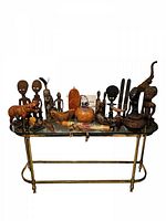 Full collection of African handcrafted wooden sculptures and figurines displayed on a glass table, showing variety of large and small items including animals, human figures, and carved bowls.