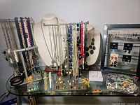 Full display of various costume jewelry pieces on necklace stands, display bars, and flat surfaces showing necklaces, rings, bracelets, watches, and earrings.