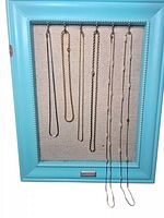 Six necklaces displayed on a blue frame with fabric backing, showing variety of chains and styles.