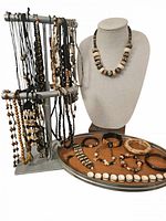 Photo showing multiple indigenous style necklaces hanging on a two-level jewelry stand, and several bracelets and a necklace displayed on a serving tray and bust. Materials appear to include wood, stone, bone and shell beads.