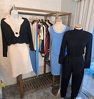 Display of black and cream blazer with skirt, blue knit dress, and black pants set with long sleeve top alongside hanging garments on rack