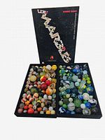 Two trays filled with colorful vintage marbles alongside a Robert Block identification guide book for marbles