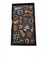 Top-down view of the lot showing 22 vintage pins and brooches placed in a tray with a grey felt base, mainly gold and silver toned metal pieces in various abstract, floral, and geometric shapes.