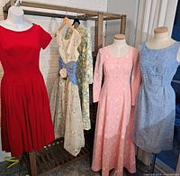 Five vintage women's dresses: red pleated short sleeve, sleeveless floral with blue waist accent, pink long-sleeve floor-length floral, and blue dress with elbow sleeves and gold floral print.