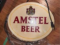 Oval Amstel Beer sign unlit on floor with power cable visible.