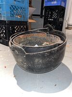 Two black cast iron caldrons with metal handles, one nested inside the other. Shows rust on interior and outer surfaces.