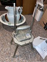 Full view of metal industrial vegetable/french fry slicer with a handle and tripod legs on carpeted floor.