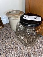 Photo showing the side view of the ceramic crock with lid and the clear glass jar with metal lid in front, placed on carpeted floor beside wooden cabinet.