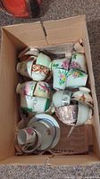 Boxed collection of assorted vintage teacups and saucers showing color variations and floral patterns.