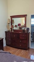 Full view of dresser and matching mirror in bedroom setting, showing dark wood finish, multiple drawers, and top mirror with frame