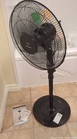 Front view of black Westinghouse 3-speed floor fan standing on tile floor with instruction manual beside it