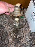 Full view of one oil lamp with clear glass base and metal burner showing wick