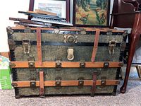 Front view of the vintage steamer trunk showing leather straps, metal latches, and wooden slats.