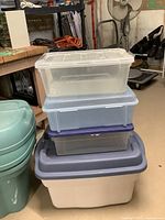 Stack of four plastic storage containers in different sizes and colors including clear and blue with lids
