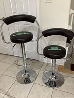 Two adjustable bar stools with dark brown faux leather seats and backs, chrome bases and footrests, shown side by side.