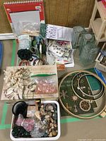 Assortment of craft supplies including rocks, beads, embroidery hoops, wire, sketch pads, and decorative storage box arranged on floor